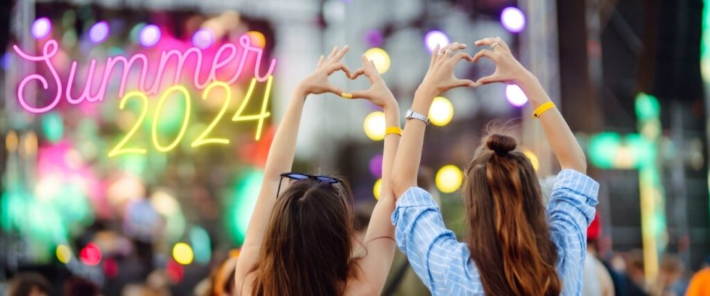 Summer 2024. Two woman with fingers in a heart shape at an outdoor summer concert.